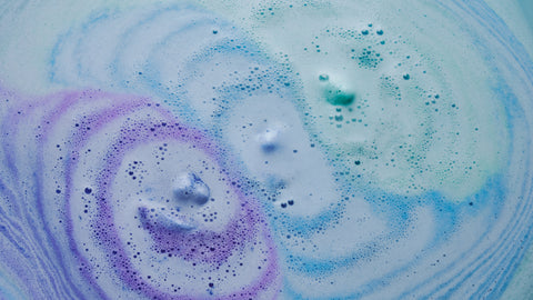 There are 3 colorful bath bombs are disolving in water, changing the color into purple, blue and green. 